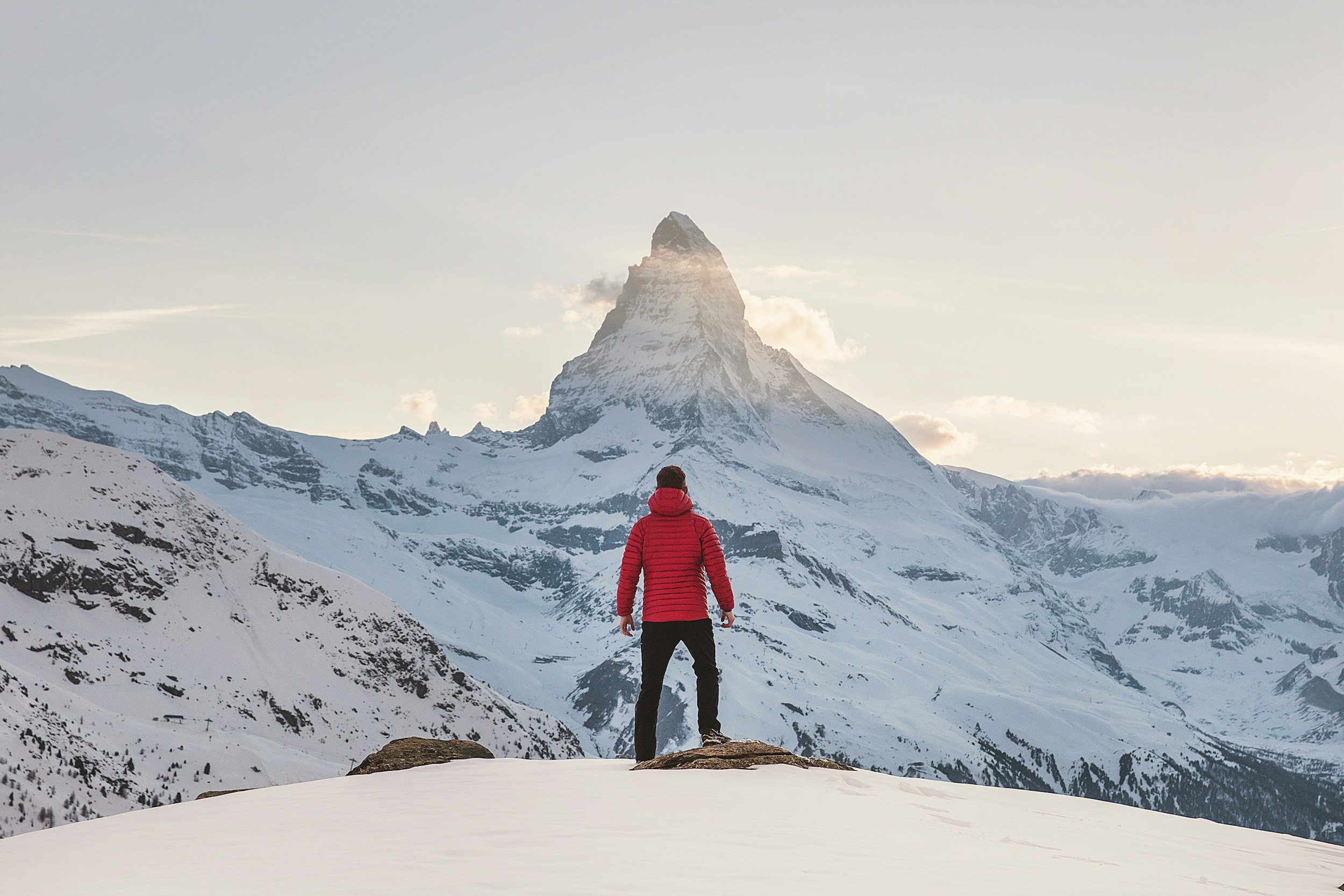 Eine Person in roter Jacke vor einem schneebedeckten Berg
