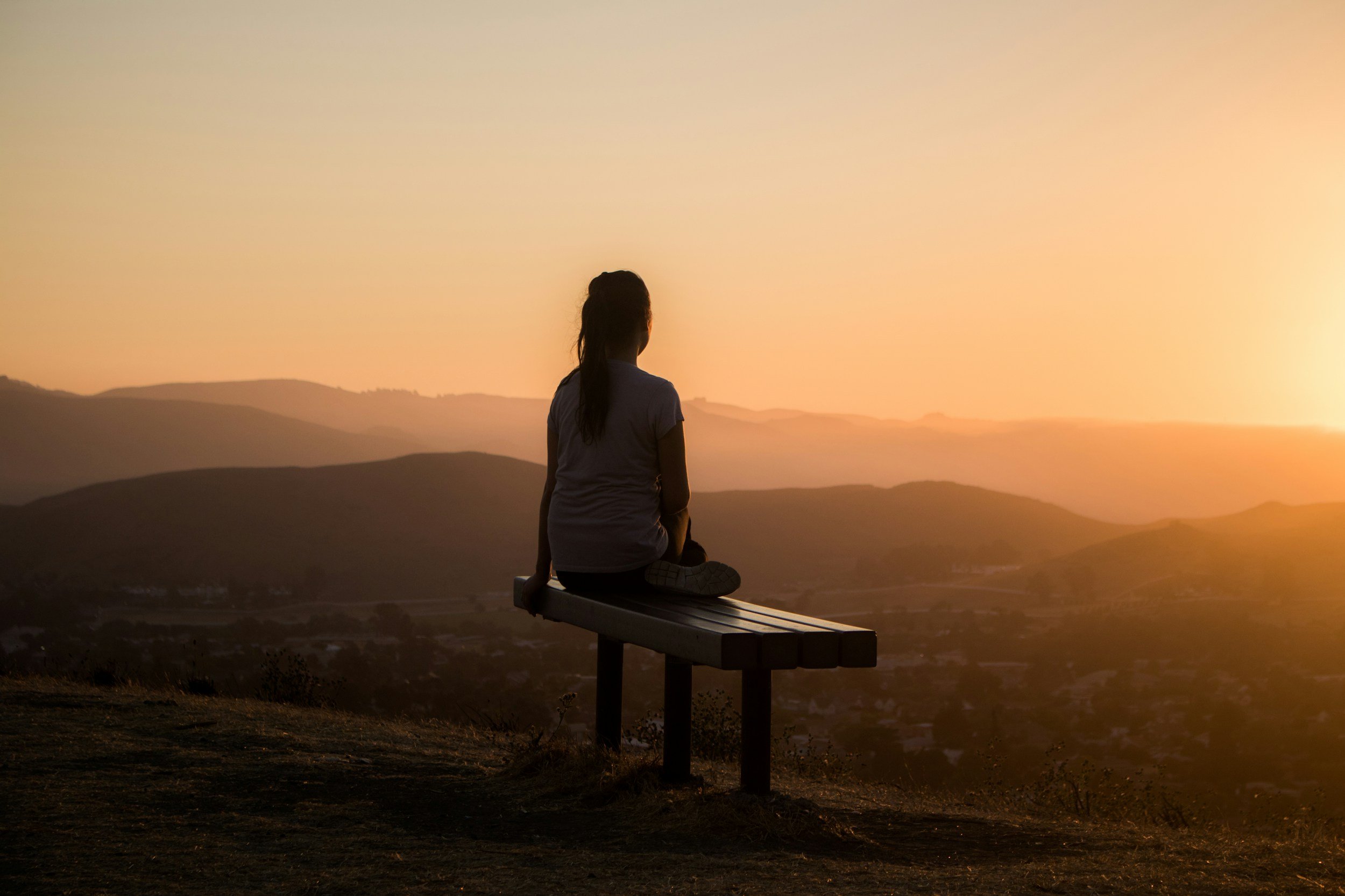 Eine Person sitzt auf einer Bank und blickt in die Berglandschaft